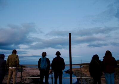 Three sets of couples, standing with a grey-blue sky, watching over a reservoir