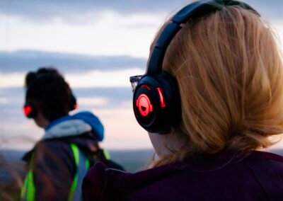 A person in a hi-vis wearing headphones leading, a close up of the back of a young womans head with ginger hair wearing headphones too.